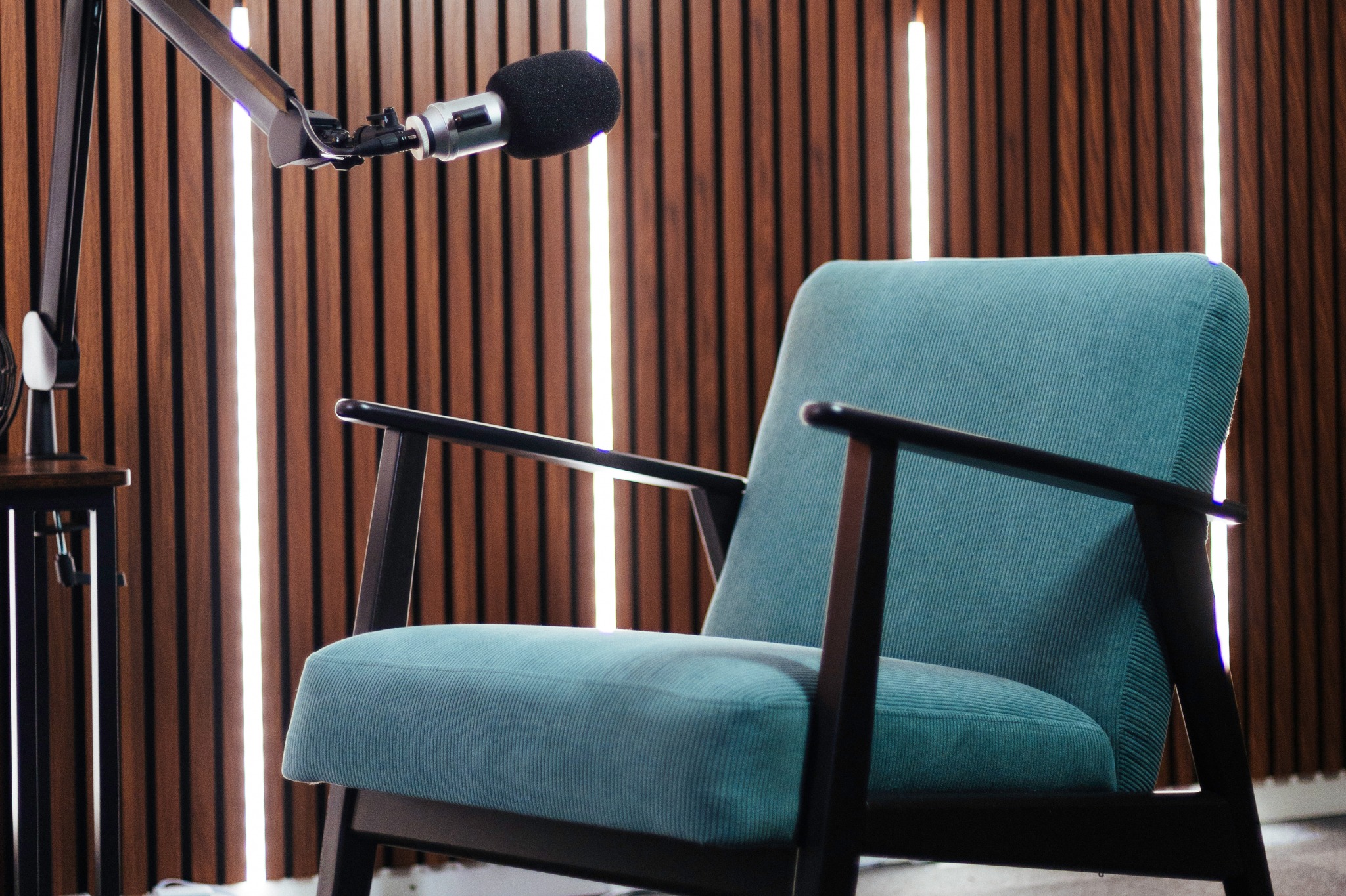 Fauteuil turquoise et microphone devant une paroi en bois éclairée par des bandes lumineuses.